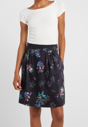 Valkoinen lyhythihainen istuva paita yhdistettynä polvipituiseen mustaan hameeseen, jossa on värikkäitä kukkakuvioita ja laskoksia.