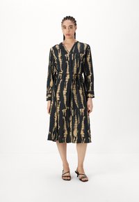 Juoda ir auksinė raštuota suknelė su ilgomis rankovėmis ir juosmens dirželiu, turinti V formos iškirptę ir plaukuojančią iki kelių sijoną. Minimalistinis dizainas.