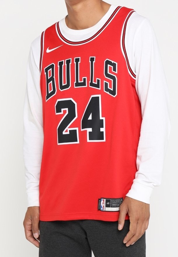 Červený basketbalový dres s nápisem "BULLS" v černé barvě na přední straně, číslem "24" pod ním a logem Nike na hrudi. Přes dres je vrstvená bílá košile s dlouhým rukávem.