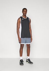 Zwart mouwloos sporttop met witte zijpanelen, gecombineerd met grijze shorts. Bevat het Adidas-logo op de borst. Draagt zwarte sneakers.