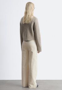 Beiger, kurzhalsiger Pullover aus weichem Material, kombiniert mit hellen, weit geschnittenen Cordhosen. Matte Textur mit subtilen Nahtdetails.