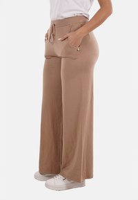 Pantaloni beige a gamba larga realizzati in tessuto morbido, con vita regolabile tramite coulisse, due tasche frontali e accessori hardware minimali.