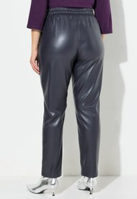 Grå fusk läderbyxor med ett stretchigt midjeband, tapered ben design och slät yta. Matchas med silverfärgade klackboots på ankeln.