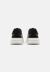 Schwarze und graue Sneaker aus Wildleder und Leder mit einer klobigen weißen Sohle und abgerundeten Akzenten an der Ferse.
