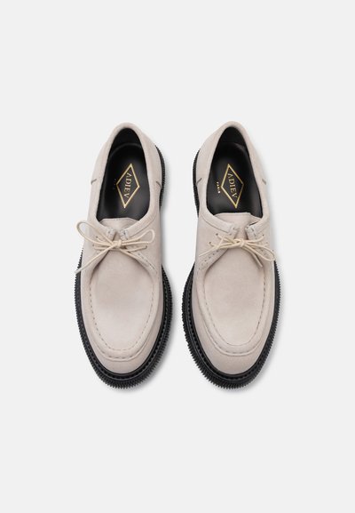 Helle graue Wildlederschuhe mit runder Zehenform, Schnürsenkeln und schwarzer Gummisohle. Sichtbare Nähte und eine glatte Textur. Markenetikett sichtbar.