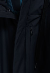 Marineblauwe jas van waterafstotende stof, slank ontwerp, met ritssluiting voorzien van een zwarte trekband en een binnenvoering met verticale strepen.