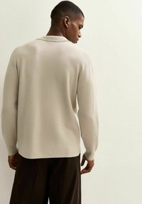 Lichtbeige pullover met een kraag, lange mouwen en een zachte textuur. Heeft een rechte snit en subtiele ribstructuren langs de halslijn.
