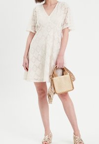 Robe en dentelle blanche avec un col en V et des manches courtes ; motif texturé ; assortie à un sac à main tissé et des sandales à talons en beige.