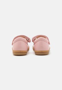 Zapatos infantiles rosas con parte superior de cuero liso, correa texturizada y suela de goma, con un talón redondeado y un diseño sencillo.