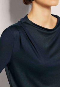 Dunkelblaues Oberteil aus einem weichen, drapierten Stoff mit glatter Textur und einem bescheidenen Ausschnitt. Leicht gepuffte Schulterdetails.