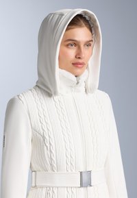 Giacca bianca con trama a trecce, dotata di cappuccio, chiusura con cerniera e cintura larga con dettaglio metallico.