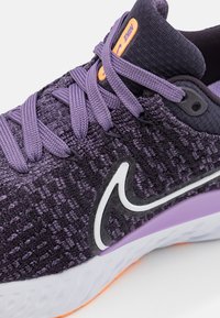 Zapatilla deportiva de punto morado con una superficie texturizada, logotipo Swoosh blanco, acentos morados y una suela intermedia blanca con una base naranja.