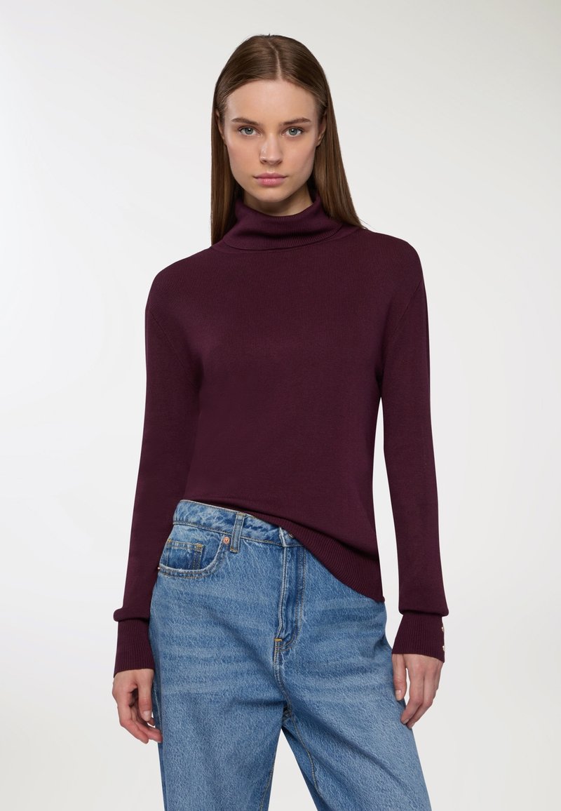 Burgundowy sweter z golfem o prążkowanej strukturze, długimi rękawami i dopasowanym kroju, w połączeniu z jasnoniebieskimi dżinsami z wysokim stanem.