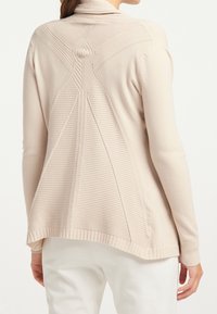 Jasnobeżowy kardigan z teksturowanymi wzorami dzianiny na plecach, z prążkowanymi mankietami i obrębem, o luźnym kroju i długich rękawach.