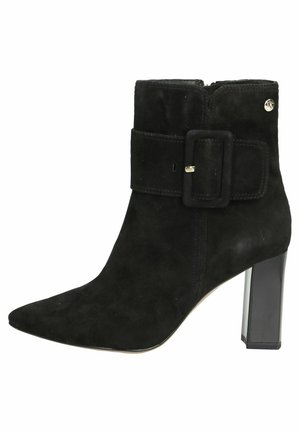 Black suede ankle boot with a pointed toe, structured design, wide fabric strap with a square buckle, and a transparent block heel.