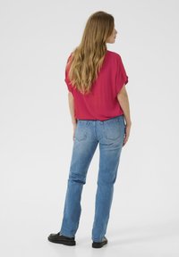 Haut magenta ample à manches courtes, associé à un jean droit bleu clair et des chaussures noires, vu de dos.