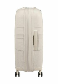 Valigia rigida di colore bianco sporco con superficie texturizzata, scanalature e maniglia laterale. Presenta due ruote nere per la mobilità.