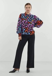 Juoda gėlėta palaidinė, papuošta spalvingais mėlynos, violetinės ir raudonos spalvų raštais, su pūstomis rankovėmis ir sagčių apykakle, derinama su juodomis kelnėmis.