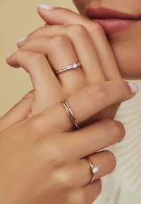 Drei roségoldene Ringe an Händen: einer hat drei kleine Edelsteine, der andere ist ein schlichter Ring, und der dritte hat ein verdrehtes Design.