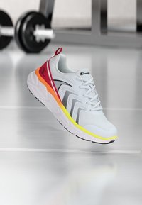 Weißer Sportschuh mit einem strukturierten Mesh-Obermaterial, schwarzen Akzenten und auffälligen roten, orangefarbenen und gelben Details an der Sohle und an der Seite.