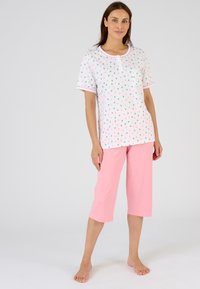 Conjunto de pijama de algodón con una blusa blanca de manga corta que presenta un colorido patrón de hojas, combinado con pantalones capri de color rosa claro.