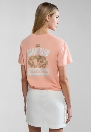 Perzikkleurig katoenen T-shirt met korte mouwen, voorzien van een grafische print op de achterkant, inclusief tekst en illustraties, gecombineerd met een witte rok.