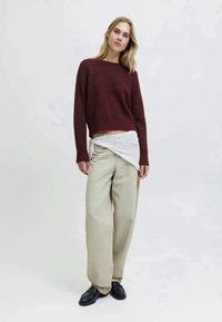 Suéter texturizado em bordeaux, calças largas em bege e um xale branco estampado. Usado com mocassins pretos. Design simples e minimalista.