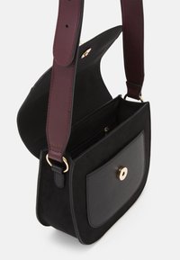 Borsa a tracolla in suede nero con una fascia in pelle bordeaux, dotata di una chiusura a scatto dorata e di una tasca interna con zip. Design pulito e minimalista.