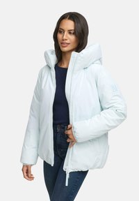 Donna che indossa un piumino azzurro chiaro sopra una maglietta blu navy e jeans, con il piumino parzialmente zipato e la mano vicino alla zip.