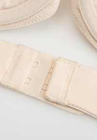 Zbliżenie zapięcia stanika na haftkę z dwoma rzędami haczyków i miękką strukturą tkaniny na jasnym tle.