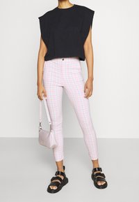 Top corto negro con mangas anchas, combinado con pantalones ajustados de cuadros rosas. Los accesorios incluyen un bolso rosa claro y sandalias negras.