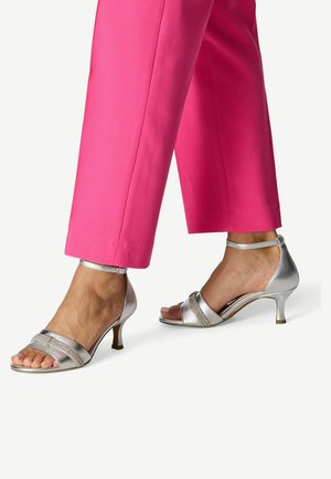Sandales argentées à talons hauts avec bout ouvert, dotées de deux lanières et d'une fine bride à la cheville. Portées avec un pantalon rose sur mesure pour le contraste.