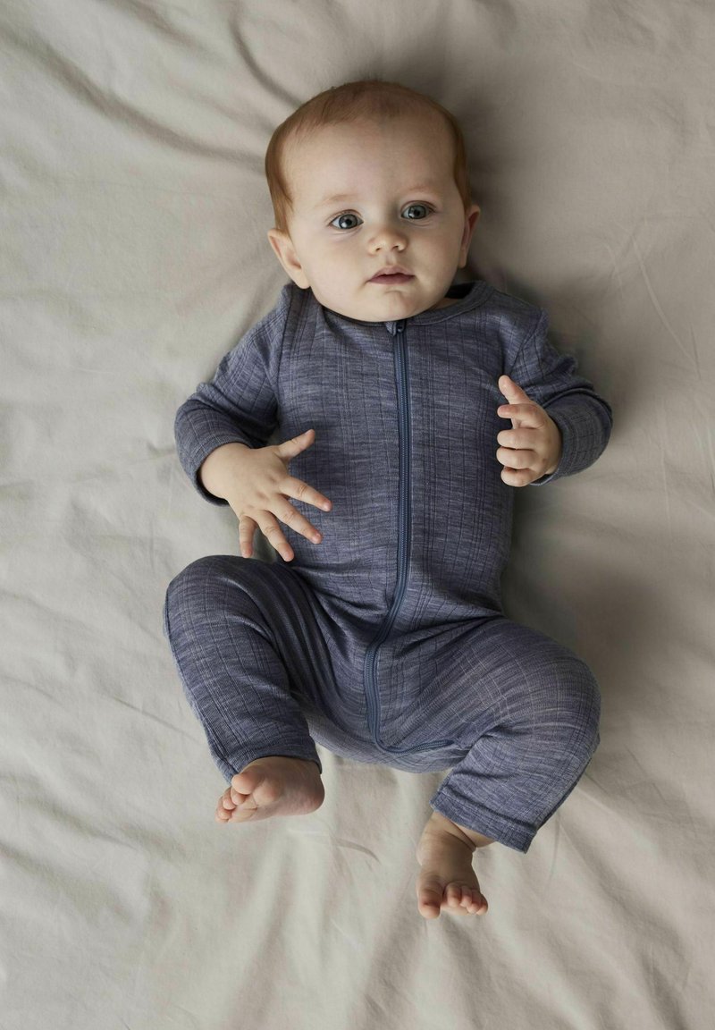 Grå zip-up babyoverall med strukturerad mönster, långa ärmar och fotsydd design. Bakgrunden är en ljusfärgad plan yta.
