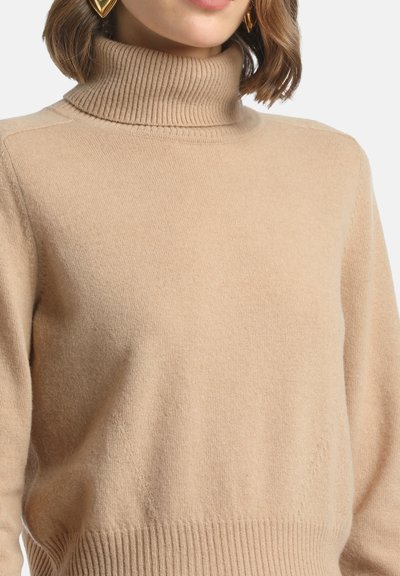 Smėlio spalvos megztinis su aukšta apykakle, pagamintas iš minkštos struktūrinės medžiagos. Turi iškilnią apykaklę ir apatinę kraštą, atpalaiduojantis siluetas, su subtiliu siuvimo detaliu.