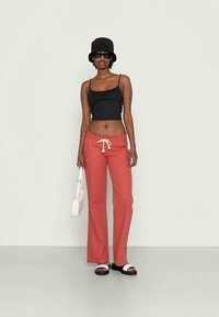 Top de tanque preto justo, calças largas corais com cordão branco, bolsa branca, chapéu tipo balde e óculos de sol pretos. Sandálias planas com detalhe em contraste.