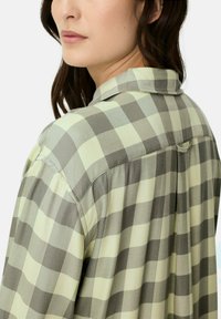 Hellgrünes und graues kariertes Hemd mit einem Kragen, Knopfdetails und weicher, gewebter Textur auf Rücken und Schultern.