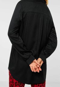 Zwart langarmshirt met een ronde zoom, zachte textuur en gegaderde mouwen. Een gladde achterkant met een eenvoudige naaddetail.