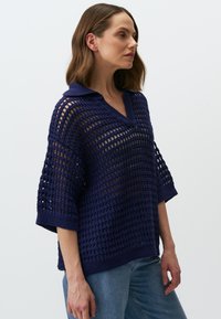 Marineblaues Strickpullover mit lockerem, offener Maschenstruktur, kurzen Ärmeln und Kragenhals. Verfügt über strukturierte Häkelmuster.