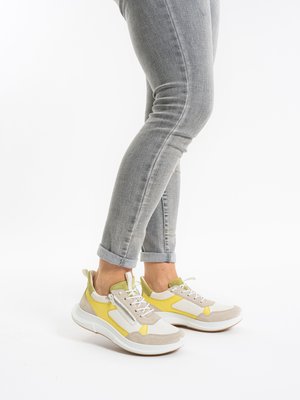 Person wearing light gray rolled-up jeans and white sneakers with yellow and beige accents against a white background.