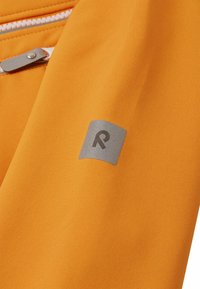 Tissu orange vif au toucher lisse. Présente un logo rectangulaire argenté avec une lettre "R" stylisée sur le côté gauche. Accent de zipper.