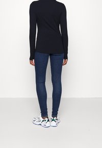 Top negro de manga larga con textura acanalada, combinado con jeans skinny azul oscuro y zapatillas blancas con acentos verdes y suelas moradas.