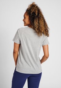 Grijze t-shirt met korte mouwen van een zachte stof, raglanmouwen en een gebogen zoom. Zichtbare stiksels langs de halslijn en zijsplitten.