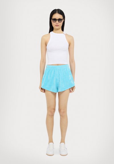 Un débardeur blanc court, un short en velours bleu clair et des baskets blanches. Des lunettes de soleil ajoutent du contraste ; le short a une taille élastique.