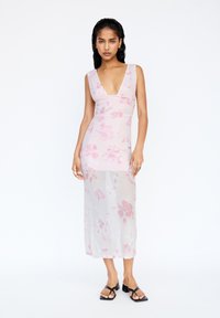 Ärmlös rosa blommig klänning med djup V-ringning, rynkad bodice, genomskinlig kjol och en figurnära silhuett. Bärs med svarta blockklack-sandaler.