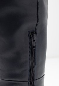 Botte en cuir bleu marine avec une fermeture éclair latérale, une texture élégante et des coutures renforcées le long des joints pour une durabilité accrue.