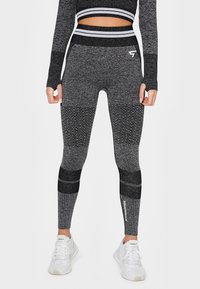 Šedé fitness legíny s texturovanými vzory, různými odstíny a vysokým pasem. Obsahují žebrované akcenty a detail loga na lýtku.