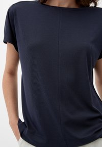 Tumman merensinisen värinen lyhythihainen paita, jossa on ribbikuvio. Ominaisuuksina rento istuvuus ja pyöristetty kaula-aukko. Taskut näkyvät sivuilla.