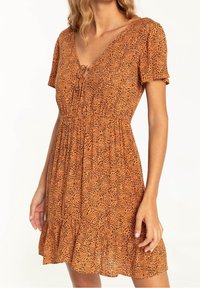 Robe orange à manches courtes avec un motif léopard, un col en V, une taille froncée et un détail de bordure à volants.
