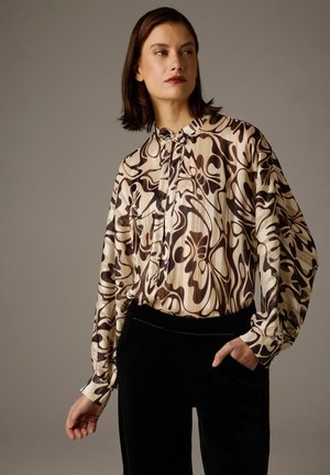 Long-sleeve blouse in cream with brown abstract patterns; features a buttoned collar and pleated design, paired with black velvet pants.