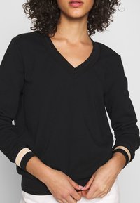 Czarna bluza z dekoltem w serek, ściągaczami z kremowymi i czarnymi paskami oraz miękką fakturą. Dopasowana z wygodnym krojem.